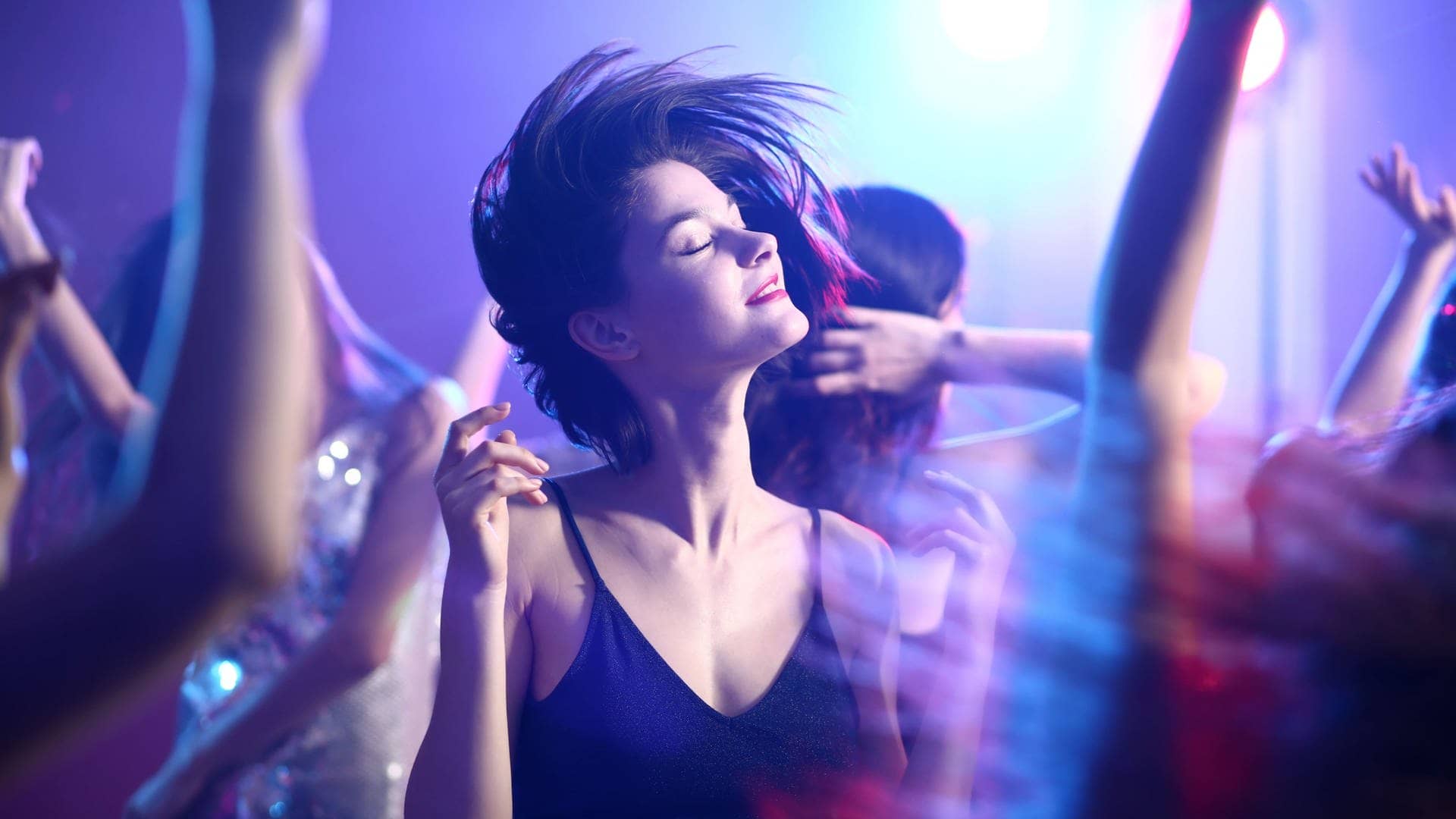 Junge F rau in Kleid tanzt mit geschlossenen Augen im Scheinwerferlicht auf einer Party (Foto: Adobe Stock, Adobe Stock/Pixel-Shot)