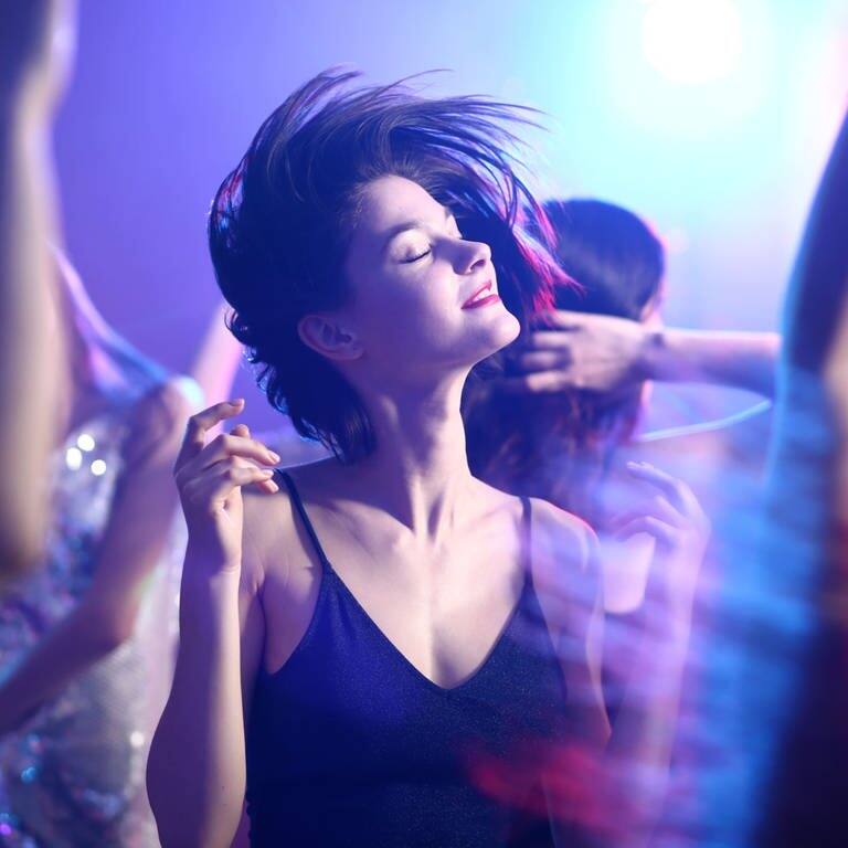 Junge F rau in Kleid tanzt mit geschlossenen Augen im Scheinwerferlicht auf einer Party (Foto: Adobe Stock, Adobe Stock/Pixel-Shot)