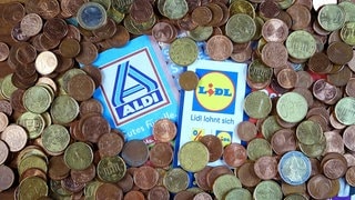 Prospekte der Discounter und Kleingeld als Symbolbild zum Thema Preissenkung, Preisanpassung, Preisoffensive, Preiskampf bei Lidl und Aldi aufgenommen am 25.05.2025 in Berlin. © BY XAMAX