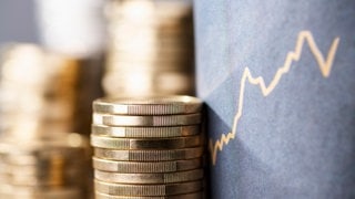 Stapel mit Münzen neben einer aufwärts gerichteten Kurve als Symbol für steigende Preise durch Inflation