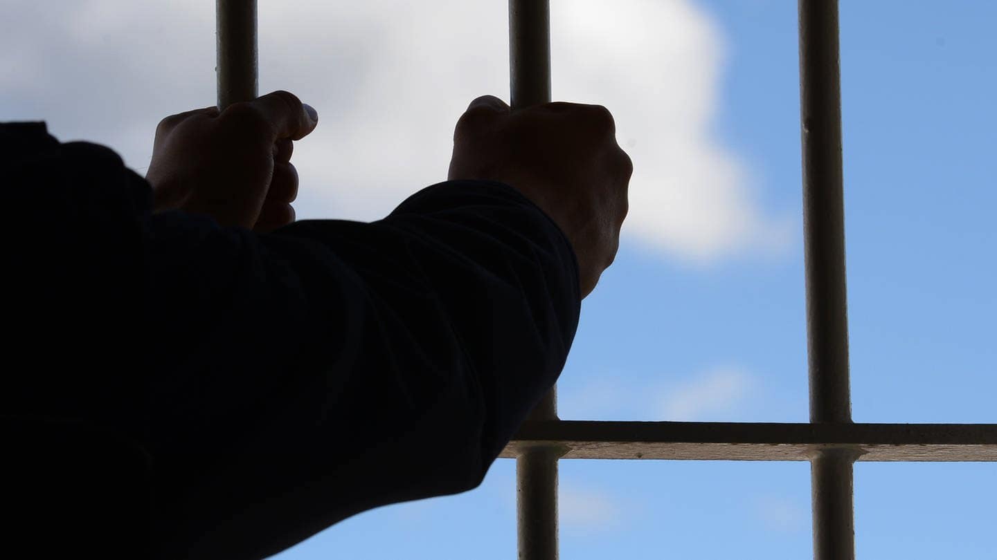 Ein Mann hält die Gitterstäbe einer Gefängniszelle fest (Foto: Patrick Seeger)