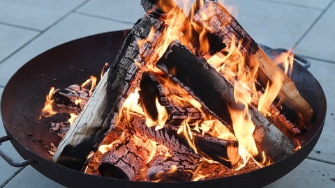 Eine Feuerschale brennt.Man sieht die Holzscheite und das Feuer. 