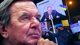 Gerhard Schröder vor durchgestrichenem Putin-Plakat