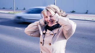 Frau steht an einer Straße und hält sich die Ohren zu