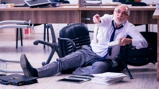 Beamter sitzt im Büro auf dem Boden und blickt verstört