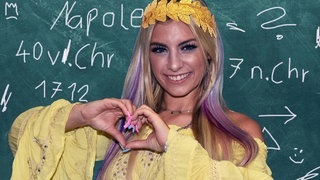 Influencer steht mit Lorbeergranz vor Schultafel