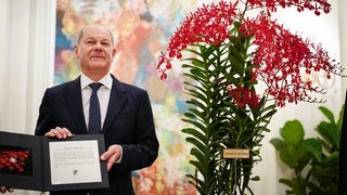 Scholz steht neben Orchidee mit dem Namen Renanthera Olaf Scholz
