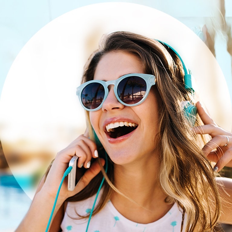 Junge Frau am Strand mit Sonnenbrille und Kopfhörern (Foto: Adobe Stock/Look!)