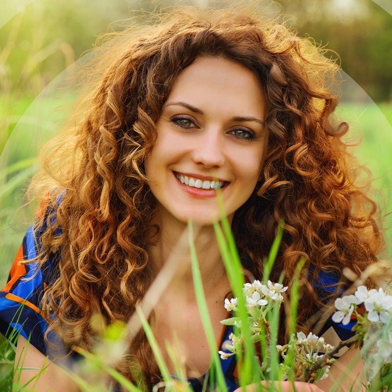 Junge Frau liegt im grünen Gras mit Blumen (Foto: Adobe Stock/Igor Link)