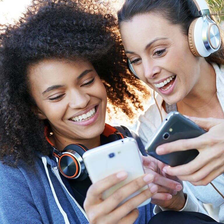 Zwei Frauen klicken auf Smartphones und hören dabei Musik. (Foto: Adobe Stock)