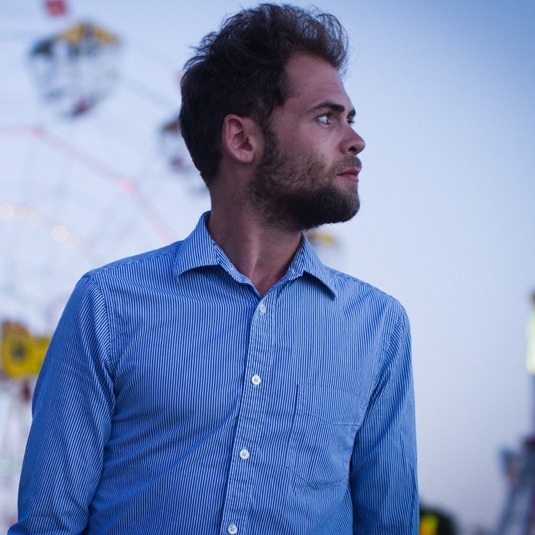 Der Singer-Songwriter Passenger trägt ein weiß-blau gestreiftes Hemd und steht vor einem Riesenrad, sein größter Hit ist „Let Her Go“ (Foto: Angelo Kehagias)