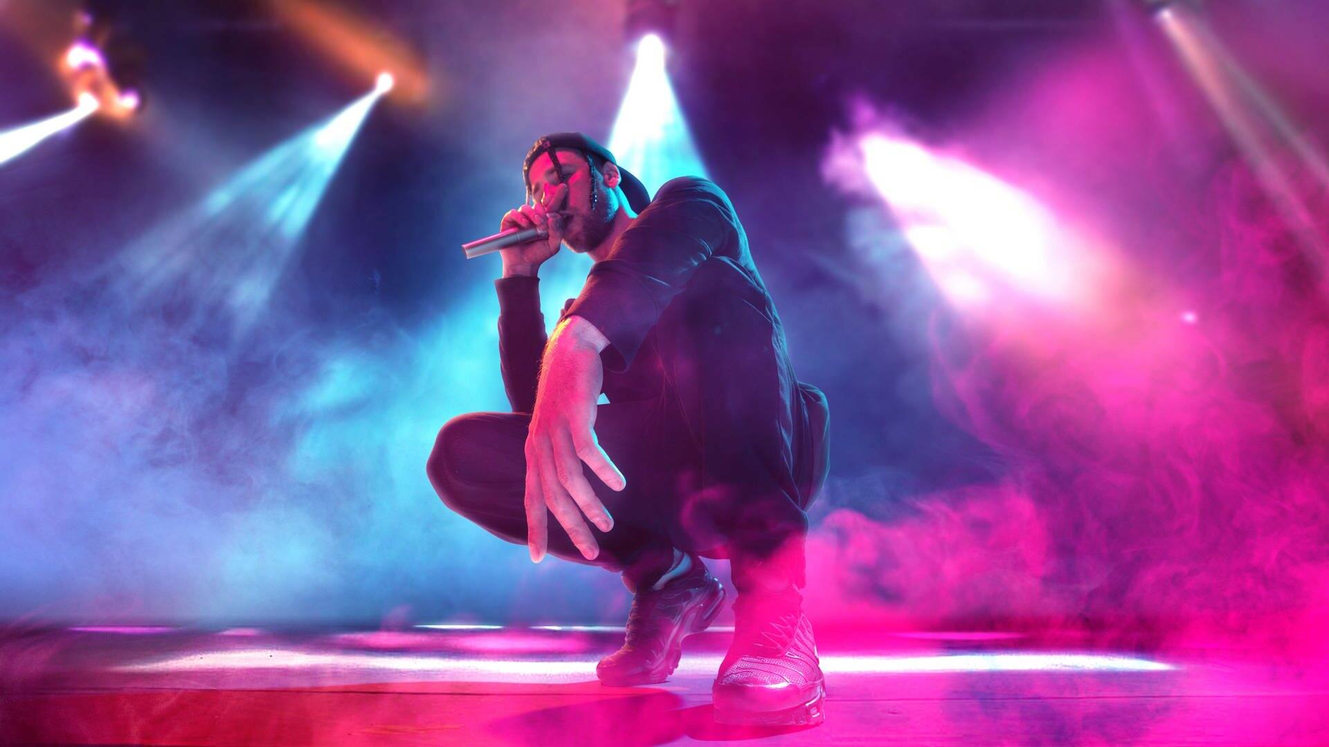 Ein Rapper ist in der Hocke und hält ein Mikrofon in der Hand (Foto: Adobe Stock, master1305)