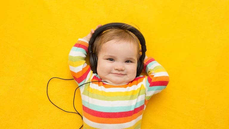 Ein Baby mit buntem Ringelpullover, das Kopfhörer trägt. Symbolisch steht das Bild für Musik, die Babies beruhigen soll.