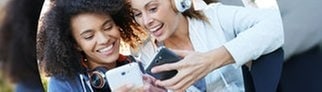 Zwei Frauen klicken auf Smartphones und hören dabei Musik.