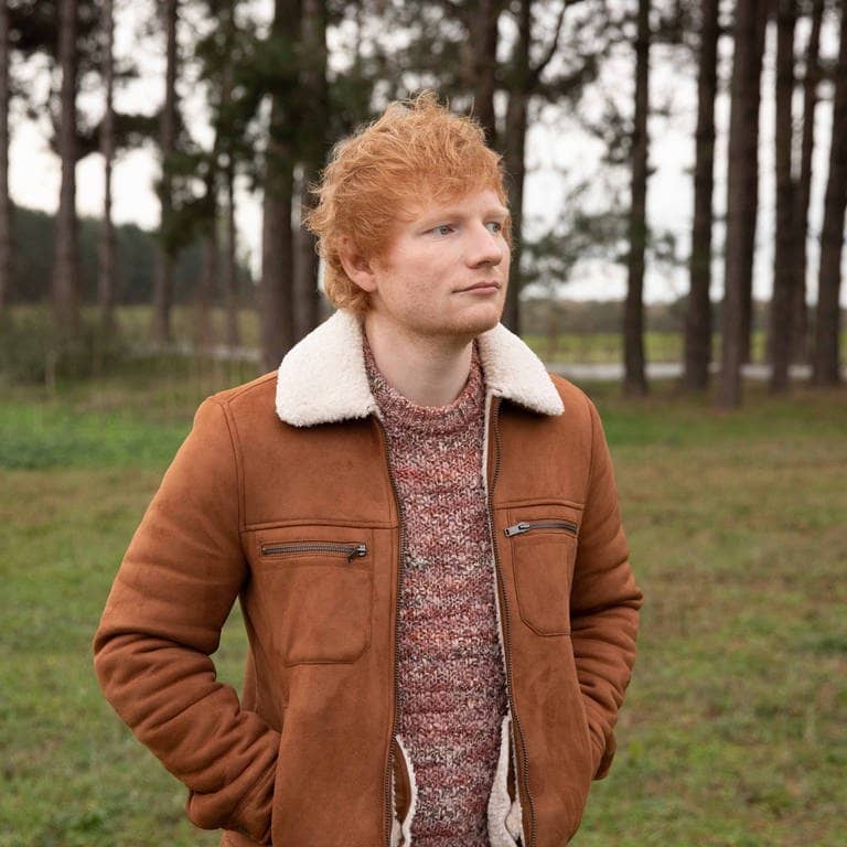 Der Sänger Ed Sheeran trägt eine braune Jacke und steht vor mehreren Bämen, er hat gerade die Doku „The Sum Of It All“ veröffentlicht (Foto: Mark Surridge)