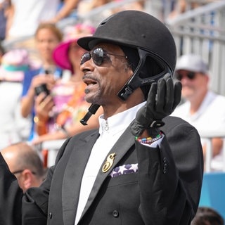 Snoop Dogg schaut sich im Reiterdress gekleidet bei den Olympischen Spielen das Dressurreiten an