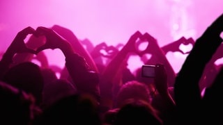 Menschen zeigen bei einem Konzert mit den Händen Herzen. Laut einer Studie macht Live-Musik uns glücklich.