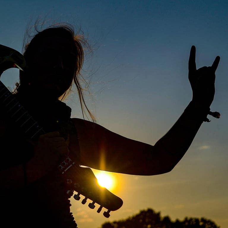 Frau mit E-Gitarre auf der Schulter zeigt den Metalgruß, die Pommesgabel. (Foto: picture alliance/Axel Heimken/dpa)
