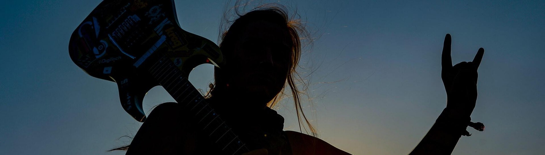 Frau mit E-Gitarre auf der Schulter zeigt den Metalgruß, die Pommesgabel. (Foto: picture alliance/Axel Heimken/dpa)