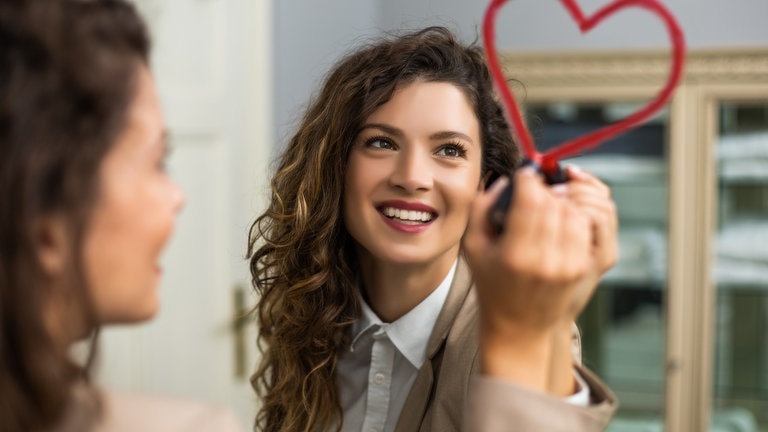 Frau schaut in Spiegel und malt mit Lippenstift ein Herz. (Foto: Adobe Stock/inesbazdar)