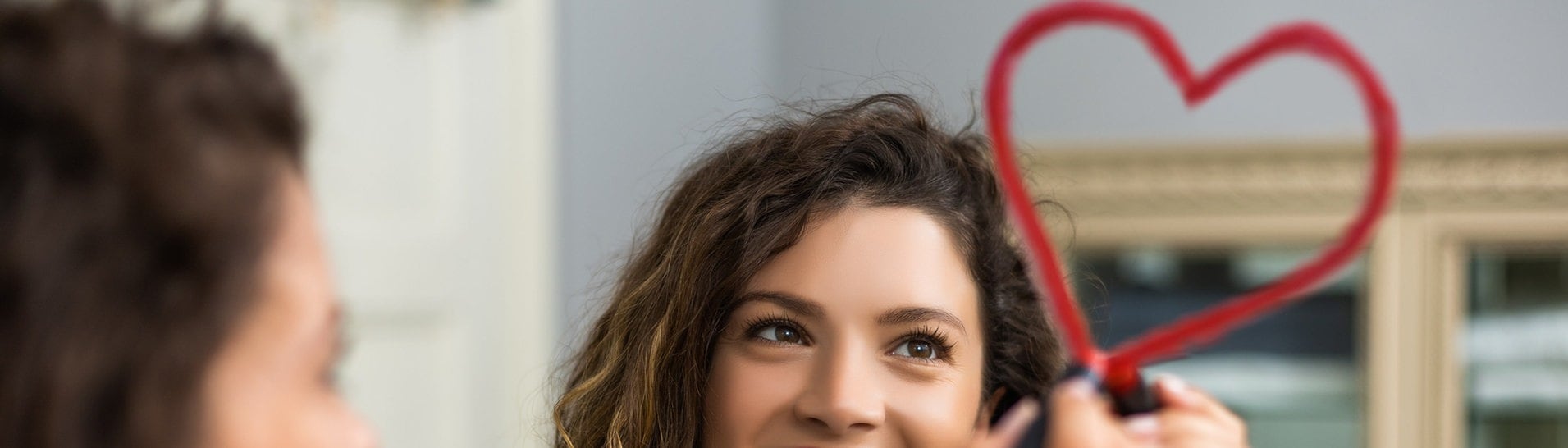 Frau schaut in Spiegel und malt mit Lippenstift ein Herz. (Foto: Adobe Stock/inesbazdar)