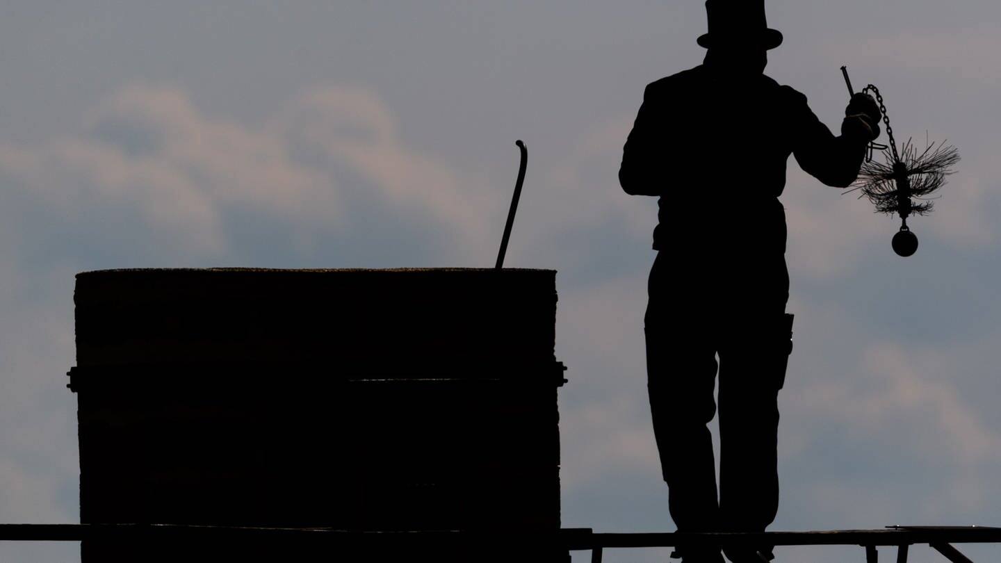 Ein Schornsteinfeger läuft mit seinem Kaminkehrerwerkzeug auf einem Dach entlang. (Foto: picture-alliance / Reportdienste, Robert Michael)