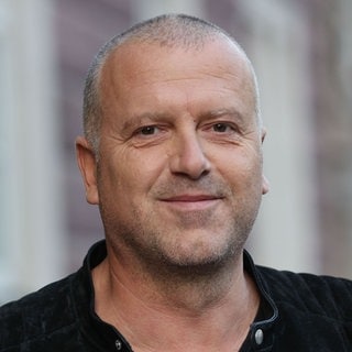 Portrait Bernhard Aichner vor Bücherregal