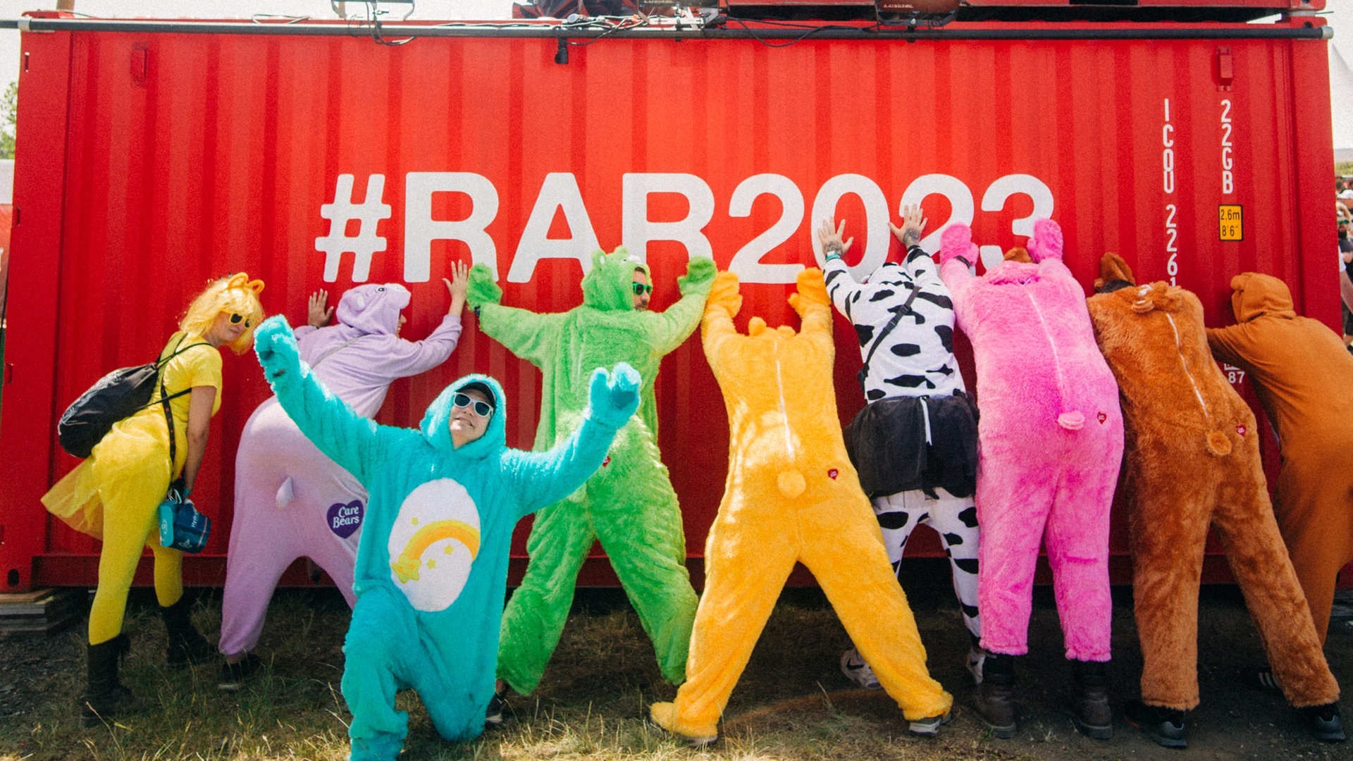 Foto: SWR3, SWR3 / Niko Neithardt Eine Gruppe steht in einer Reihe verkleidet mit bunten Kostümen an einem Container bei Rock am Ring mit dem Rücken zur Kamera (Foto: SWR3, SWR3 / Niko Neithardt)