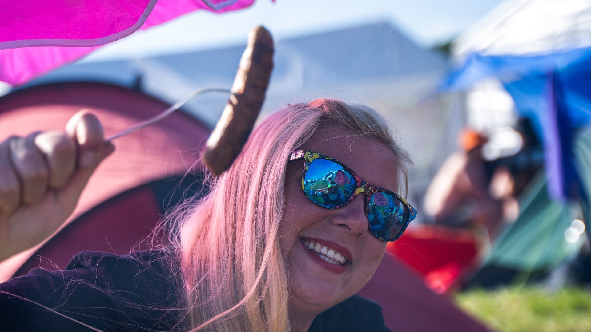 Foto: SWR3, SWR3 / Ronny Krautz Eine junge Frau hält eine gegrillte Wurst hoch und sitzt auf einem Campingstuhl bei Rock am Ring (Foto: SWR3, SWR3 / Ronny Krautz)