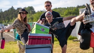 Eine junge Frau und drei Männer sind beladen mit Bierdosen und Kühlboxen auf dem Campingplatz von Rock am Ring unterwegs (Foto: SWR3, SWR3 / Ronny Krautz) Eine junge Frau und drei Männer sind beladen mit Bierdosen und Kühlboxen auf dem Campingplatz von Rock am Ring unterwegs