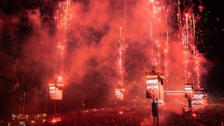 Ein rotes Feuerwerk bei Rock am Ring. Auf den LED-Leinwänden wird Linkin Park als Headliner 2026 bekannt gegeben.