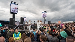 Die Band Kraftklub steht auf der Bühne umringt von Menschen und spielt 15 Minuten in der Nähe der Mandora Stage bei Rock am Ring. (Foto: picture-alliance / Reportdienste, Eibner-Pressefoto/Daniel REINELT) Die Band Kraftklub steht auf der Bühne umringt von Menschen und spielt 15 Minuten in der Nähe der Mandora Stage bei Rock am Ring.