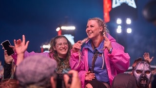 Zwei junge Frauen tragen pinke Regenponchos bei Rock am Ring und feiern in der Menge.