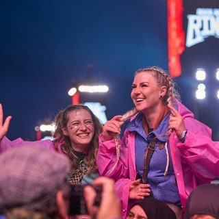 Zwei junge Frauen tragen pinke Regenponchos bei Rock am Ring und feiern in der Menge.