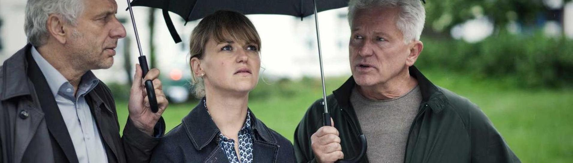 Franz Leitmayr, Christine Lerch und Ivo Batic stehen unter ihren Regenschirmen und fragen sich, Wer Ben Schröder auf dem Gewissen hat? (Foto: BR/X Filme/Hagen Keller)