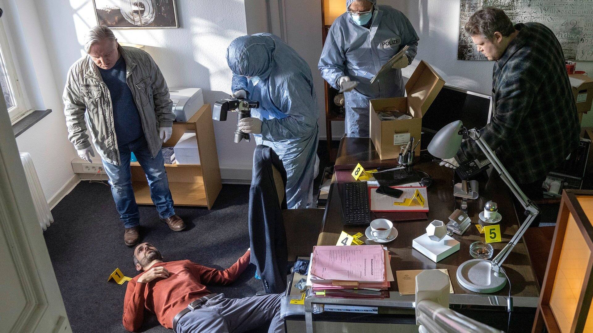 Draufsicht: Ein Toter liegt am Boden eines Büros, Kommissar Thiel steht vor ihm, weitere Polizeibeamte sind im Raum. (Foto: ard-foto s2-intern/extern, WDR/Thomas Kost)