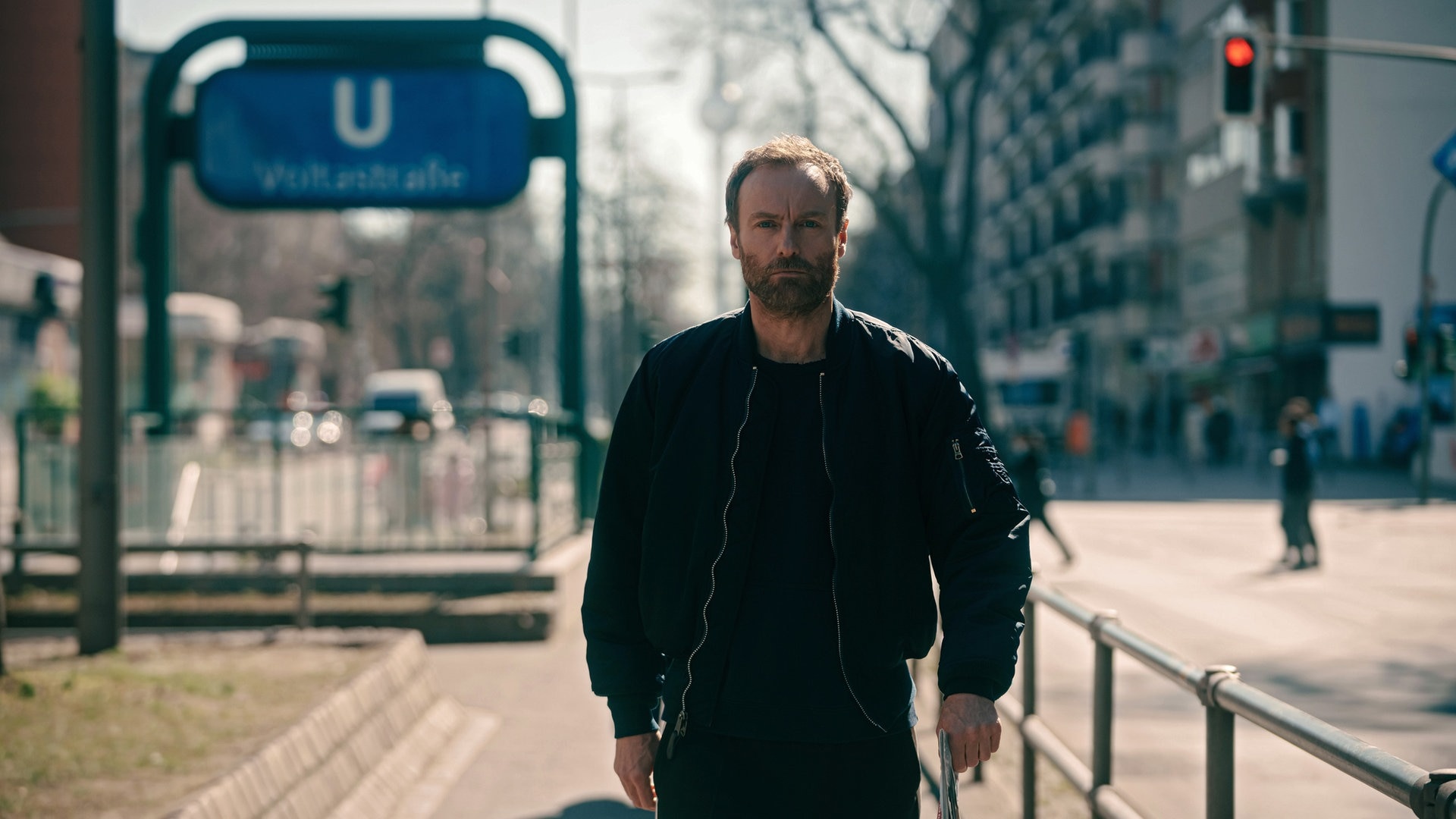 Kommissar Karow aus dem Tatort läuft auf einer Strasse durch Berlin, im Hintergrund eine U-Bahn-Station. (Foto: ard-foto s2-intern/extern, rbb/Stefan Erhard)