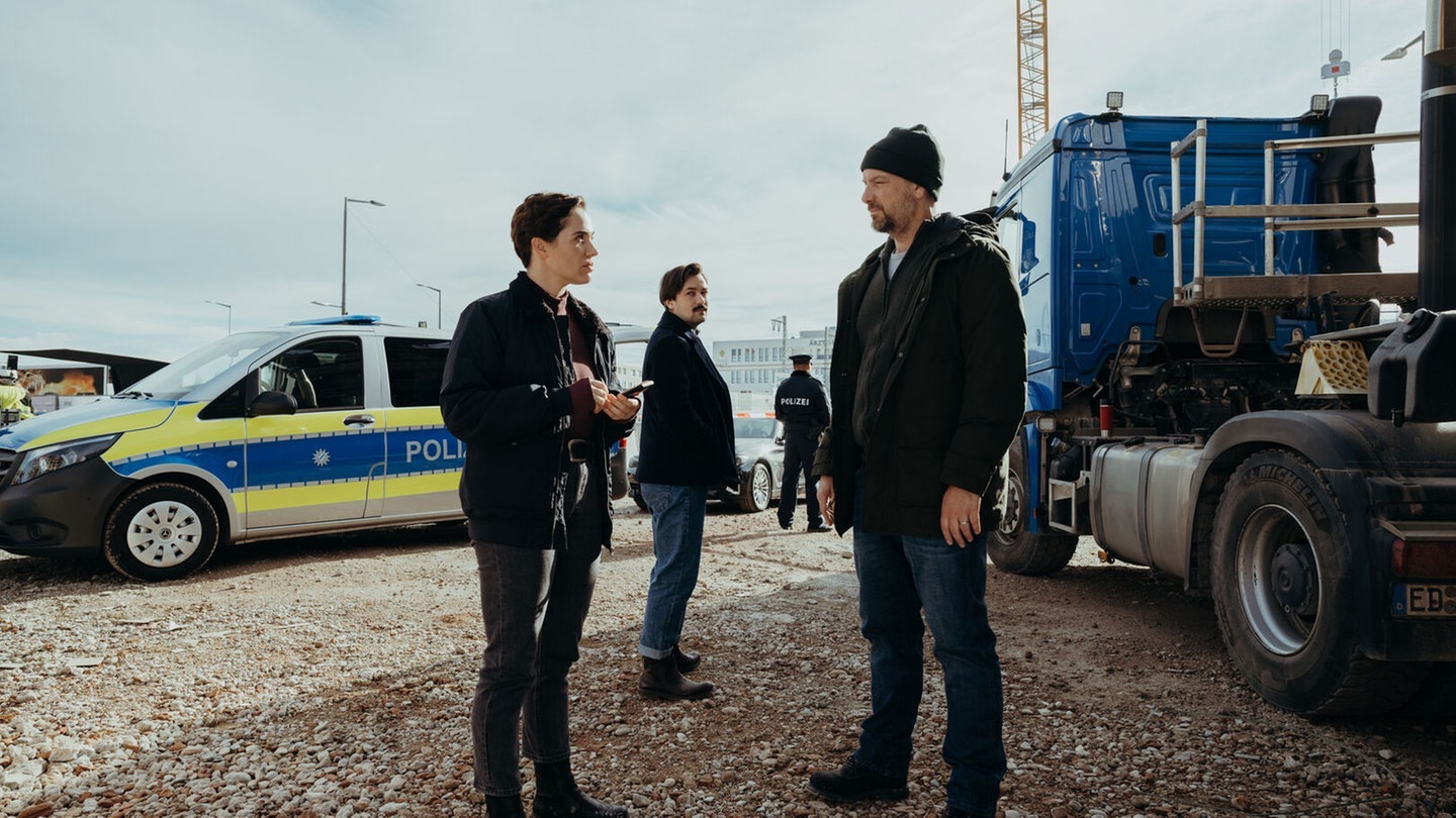 Foto: BR/Amalia Film und Dragonbird Films/Sabine Finger Die beiden Ermittler Eickhoff und Eden stehen im Polizeiruf 110 aus München zwischen einem Polizeiwagen und und einem LKW (Foto: BR/Amalia Film und Dragonbird Films/Sabine Finger)