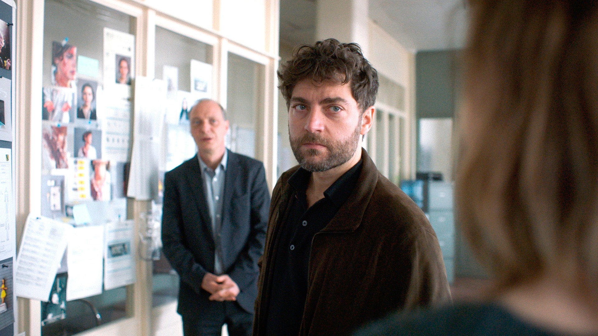 Foto: ard-foto s2-intern/extern, MDR Tatort-Kritik Dresden „Was ihr nicht seht“: Der Staatsanwalt schau im Büro mit ernstem Blick in die Kamera. Hinter ihm steht Schnabel (Foto: ard-foto s2-intern/extern, MDR)