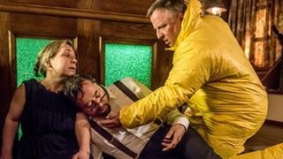 Boerne schwebt in Lebensgefahr: Können seine Assistentin Silke Haller und Kommissar Frank Thiel im Schutzanzug rechtzeitig helfen? (Foto: © WDR/Willi Weber) Boerne schwebt in Lebensgefahr: Können seine Assistentin Silke Haller und Kommissar Frank Thiel im Schutzanzug rechtzeitig helfen?