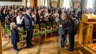 Feierstunde in der Universität: Dekan Prof. Krone (Michael Prelle, vorne links) gratuliert Prof. Boerne (Jan Josef Liefers, vorne rechts) zum neuen Forschungsauftrag – auch Boernes Assistentin Silke H (Foto: © WDR/Willi Weber) Feierstunde in der Universität: Dekan Prof. Krone (Michael Prelle, vorne links) gratuliert Prof. Boerne (Jan Josef Liefers, vorne rechts) zum neuen Forschungsauftrag – auch Boernes Assistentin Silke H
