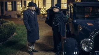 Kommissare Batic und Leitmayr stehen in Verkleidung neben einem Auto und begrüßen sich