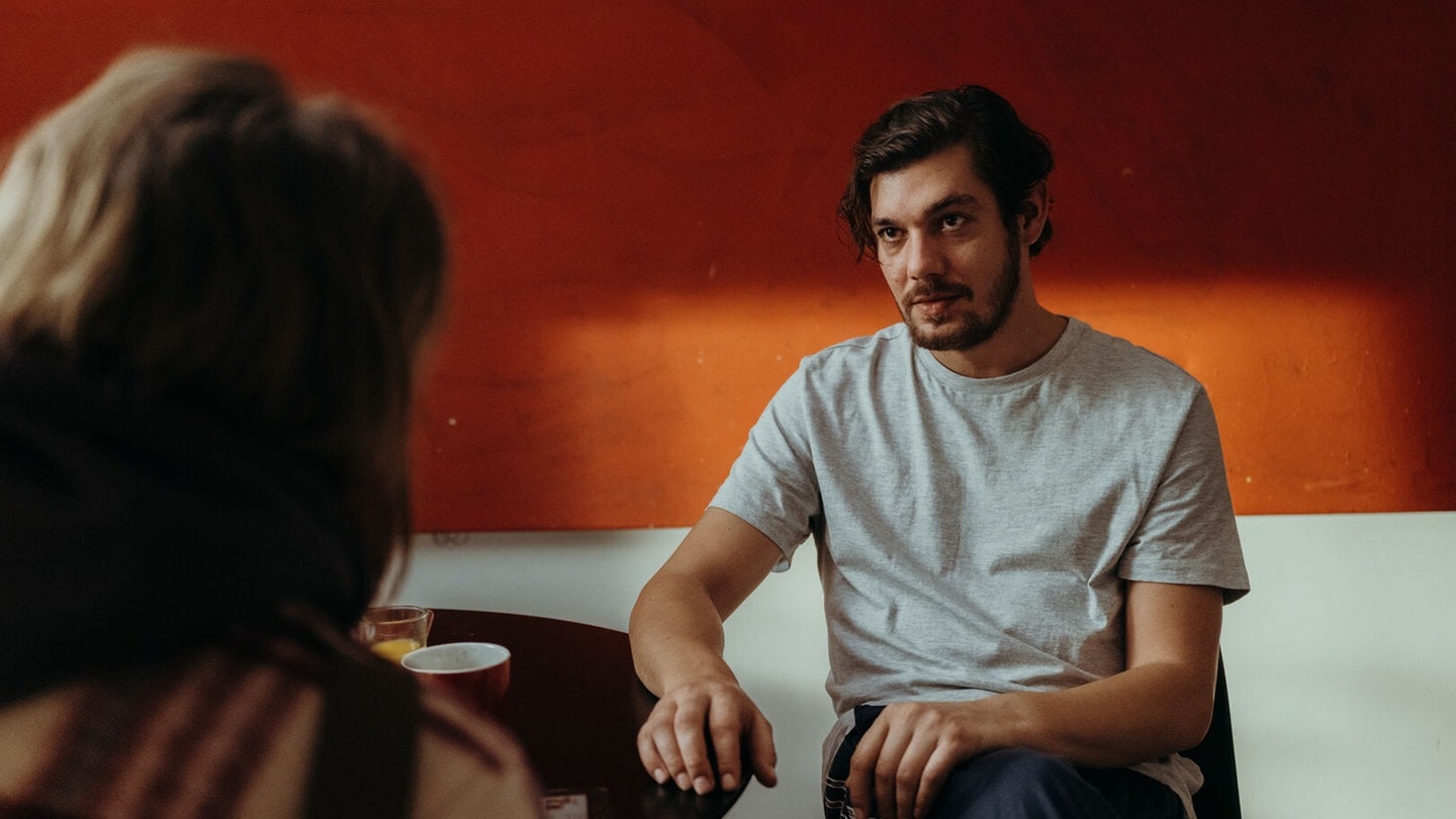 Ein junger Mann sitzt in einer Szene des Polizeiruf 110 aus München an einem Tisch (Foto: BR/Amalia Film und Dragonbird Films/Sabine Finger)