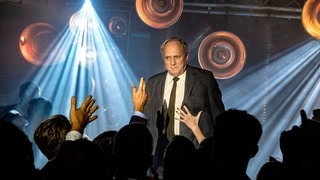 Tatort-Kritik Wiesbaden „Murot und das Paradies“: Felix Murot auf einer Bühne vor vielen Leuten (Foto: ard-foto s2-intern/extern, HR / Bettina Müller) Tatort-Kritik Wiesbaden „Murot und das Paradies“: Felix Murot auf einer Bühne vor vielen Leuten