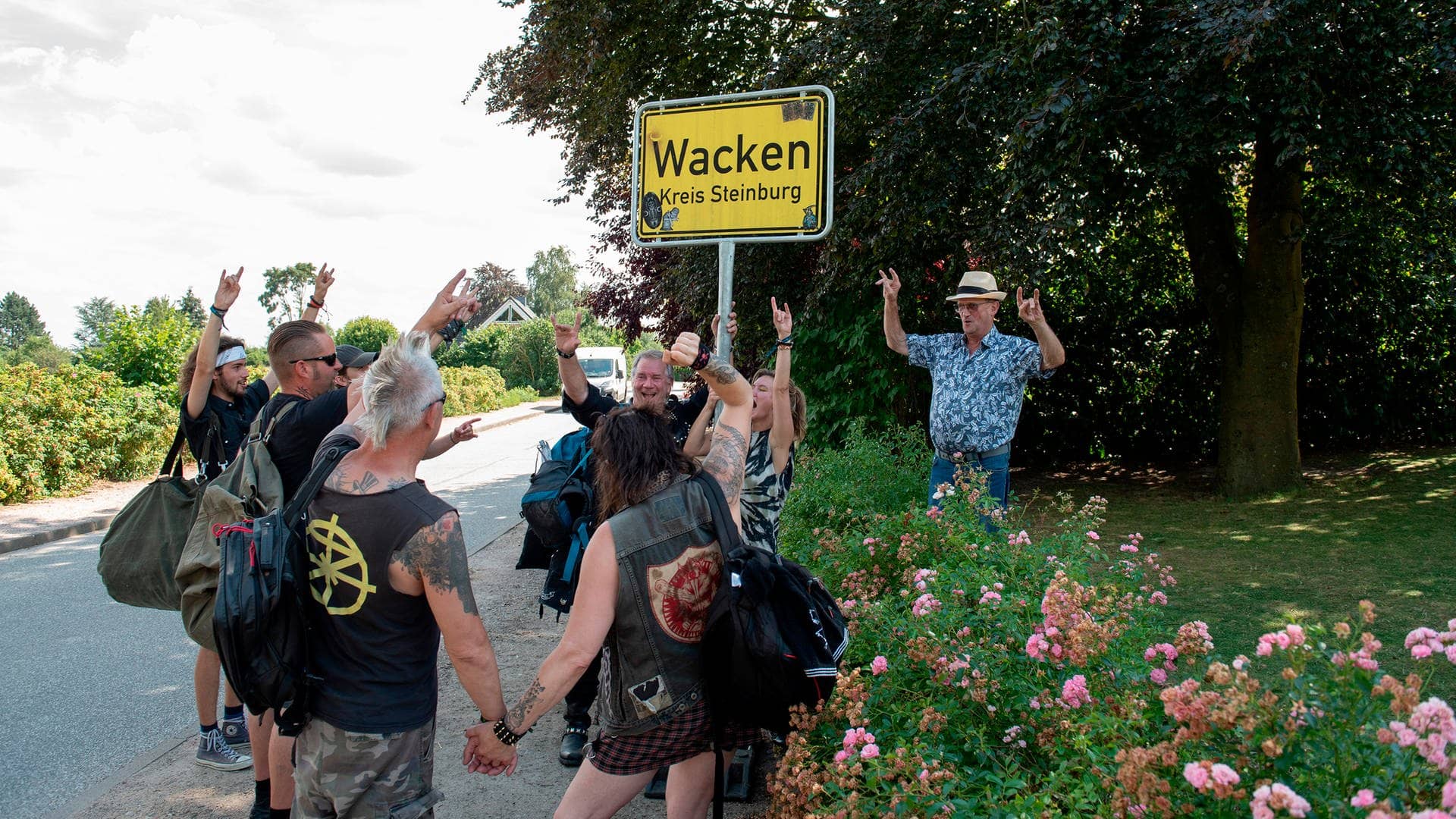 Tatort-Kritik Kiel „Borowski und das unschuldige Kind von Wacken“: Wacken Fans feiern vor dem Ortsschild des Dorfes Wacken