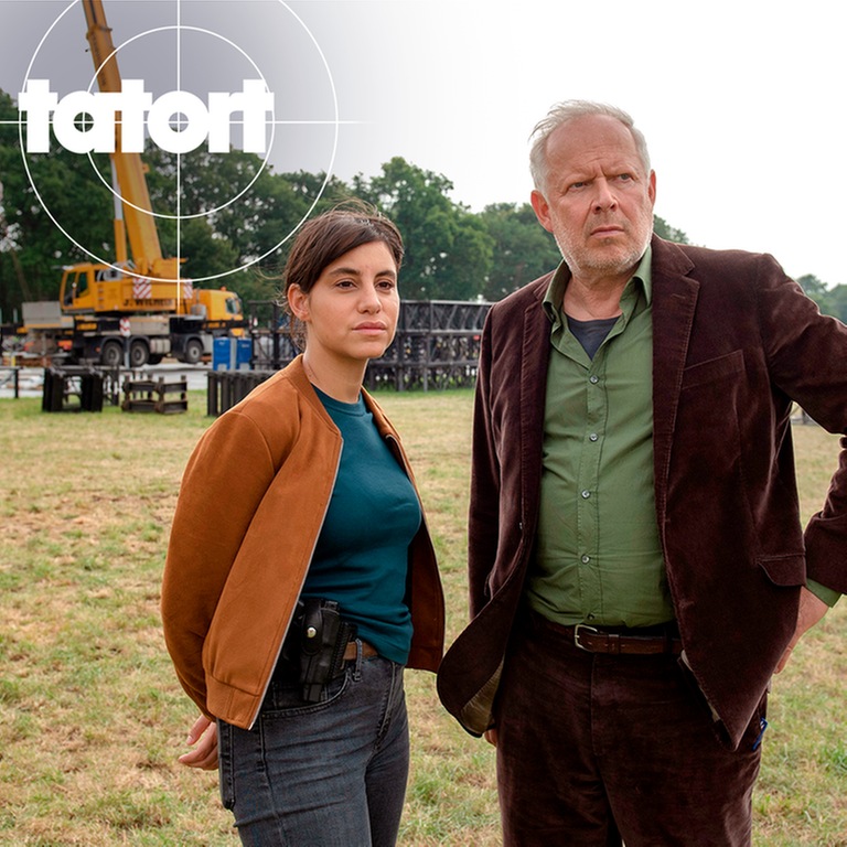 Tatort-Kritik Kiel „Borowski und das unschuldige Kind von Wacken“: Die beiden Kommissare im Vordergrund im Hintergrund der Aufbau des Gerüstes der Bühne des Wacken Open-Air (Foto: ard-foto s2-intern/extern, NDR / Thorsten Jander)