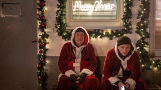 Tatort-Kritik aus Köln „Des anderen Last“: Ein alter und ein junger Mann sitzen in Weihnachtsmann-Kostümen auf einer Bank.