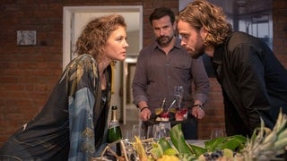 Tatort-Kritik „Borowski und der Wiedergänger“ aus Kiel: Ein Paar schaut sich ernst über einen Esstisch an, im Hintergrund ein Mann mit Geschirr in der Hand (Foto: ard-foto s2-intern/extern, NDR / Thorsten Jander) Tatort-Kritik „Borowski und der Wiedergänger“ aus Kiel: Ein Paar schaut sich ernst über einen Esstisch an, im Hintergrund ein Mann mit Geschirr in der Hand