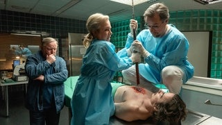 Silke „Alberich“ Haller (Christine Urspruch) und Dr. Karl-Friedrich Boerne (Jan Josef Liefers) leisten in der Gerichtsmedizin Schwerstarbeit, um den Leichnam von Anwalt Oskar Weintraub (Nils Bunkhorst) von der skurrilen Todesursache – einem alten Speer – zu befreien. Hauptkommissar Frank Thiel (Axel Prahl) kann nur zögerlich zusehen, da der Anblick starken Nerven bedarf. | Tatort-Kritik aus Münster: „Man stirbt nur zweimal“ (Foto: ard-foto s2-intern/extern, WDR/Thomas Kos) Silke „Alberich“ Haller (Christine Urspruch) und Dr. Karl-Friedrich Boerne (Jan Josef Liefers) leisten in der Gerichtsmedizin Schwerstarbeit, um den Leichnam von Anwalt Oskar Weintraub (Nils Bunkhorst) von der skurrilen Todesursache – einem alten Speer – zu befreien. Hauptkommissar Frank Thiel (Axel Prahl) kann nur zögerlich zusehen, da der Anblick starken Nerven bedarf. | Tatort-Kritik aus Münster: „Man stirbt nur zweimal“