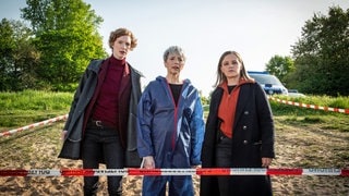 Szenenbild Tatort „Solange du atmest“ aus Bremen: Die Bremer Ermittlerinnen Linda Selb und Liv Moormann stehen mit der Gerichtsmedizinerin vor einem Absperrband am Tatort. (Foto: ard-foto s2-intern/extern, Radio Bremen / Claudia Konerding) Szenenbild Tatort „Solange du atmest“ aus Bremen: Die Bremer Ermittlerinnen Linda Selb und Liv Moormann stehen mit der Gerichtsmedizinerin vor einem Absperrband am Tatort.